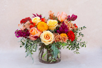 Lush garden arrangement in a glass vase with bright and colorful flowers.